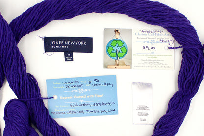 A skein of Vegan, Purple, 62% Cotton, 38% Acrylic, DK Weight yarn encircling the sweater labels it was recycled from, as well as the hand written yarn tags detailing the specs of this recycled yarn to help you make your next project! 