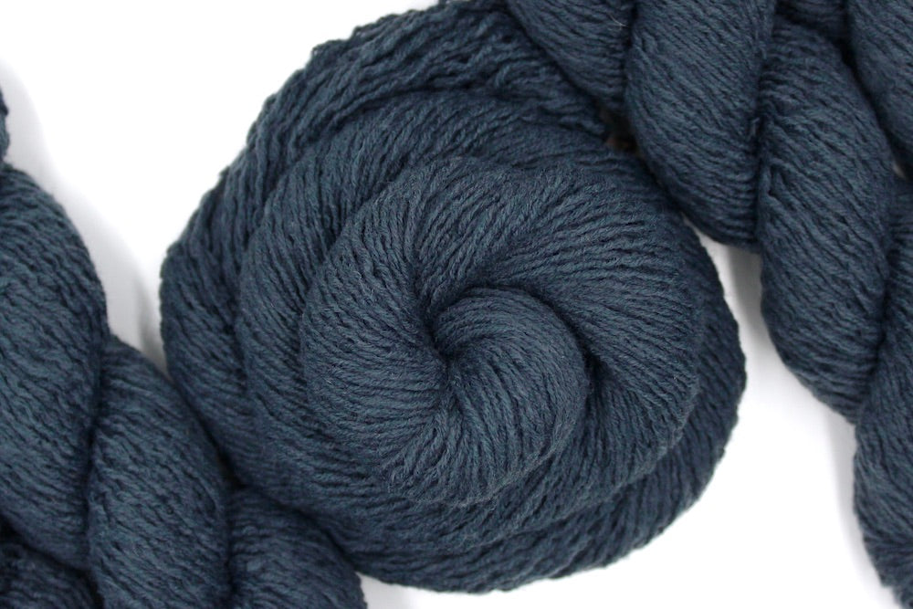 A skein of dark grey sport weight Yarn recycled by hand from unwanted sweaters swirled attractively in the center of the frame. 