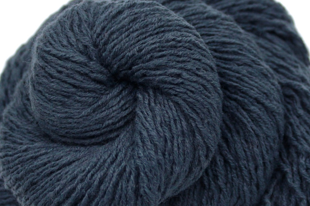 A close up shot of a skein of dark grey sport weight Yarn recycled by hand from unwanted sweaters beautifully coiled in the center of the frame.
