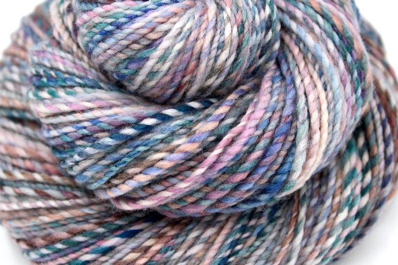 A close up view of a one of a kind, hand dyed variegated skein of multicolored Blue, Teal, Pink, Brown and Tan self-striping wool Yarn. 