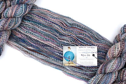 A one of a kind, hand dyed variegated skein of multicolored Blue, Teal, Pink, Brown and Tan self-striping wool Yarn draped diagonally across the frame, so you can really see the color play. 