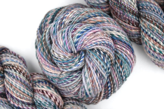 A one of a kind, hand dyed variegated skein of multicolored Blue, Teal, Pink, Brown and Tan self-striping wool Yarn coiled attractively in the center of the frame. 