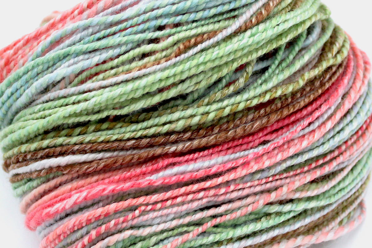A close up view of a one of a kind, hand dyed gradient skein of multicolored Pink, Blue, Green, Tan, and Brown self-striping wool Yarn. 