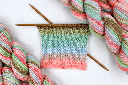A sample swatch knitted from a one of a kind, hand dyed gradient skein of multicolored Pink, Blue, Green, Tan, and Brown self-striping wool Yarn. 
