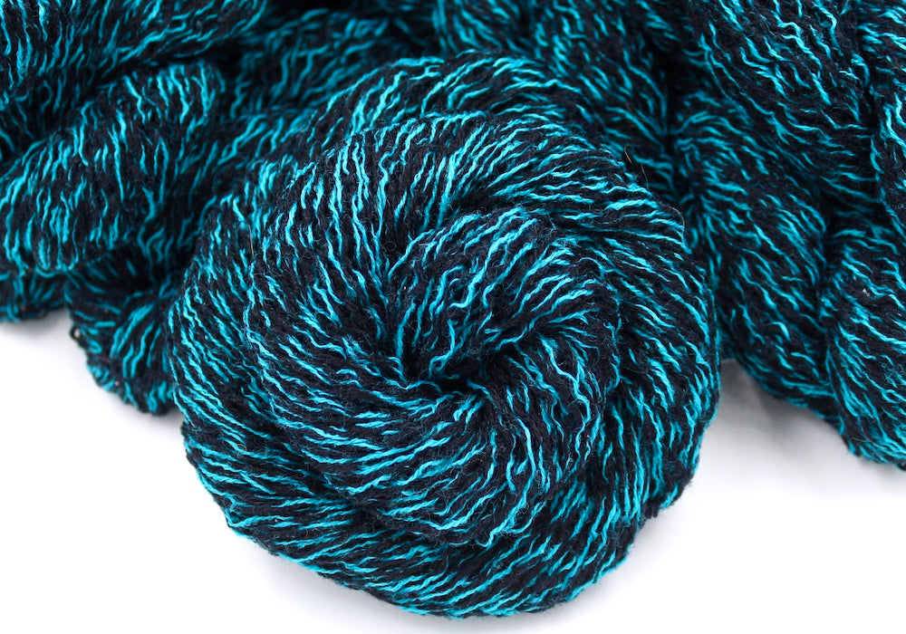 Several skeins of black and blue sport weight recycled by hand from unwanted sweaters stacked on top of each other attractively. 