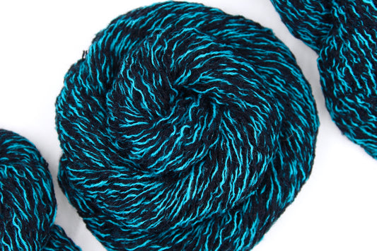 A skein of black and blue sport weight Yarn recycled by hand from unwanted sweaters swirled attractively in the center of the frame. 