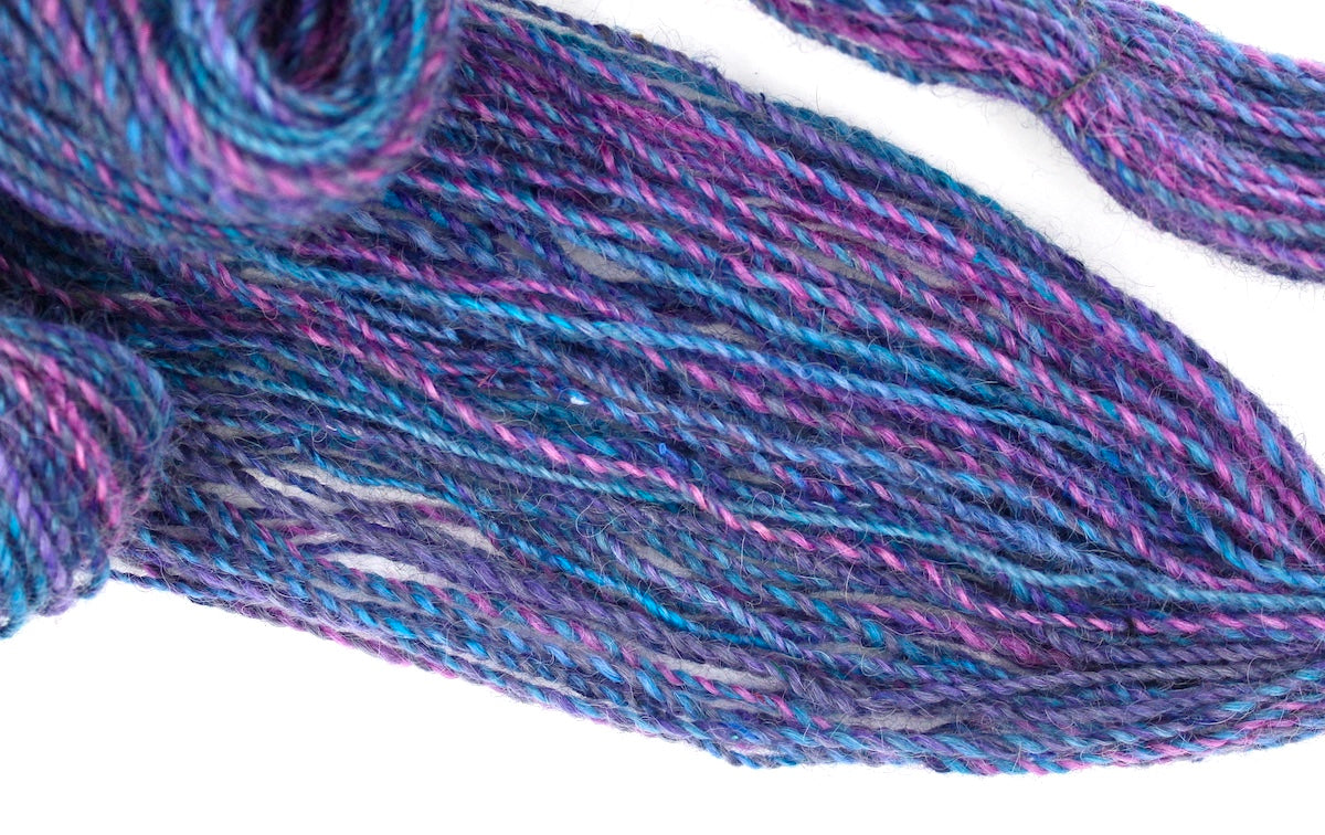A one of a kind, hand dyed Variegated skein of multicolored Hot Pink, Blue, and Purple self-striping wool Yarn draped diagonally across the frame, so you can really see the color play. 