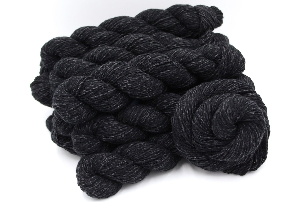 Several skeins of black and grey, DK weight recycled by hand from unwanted sweaters stacked on top of each other attractively. 