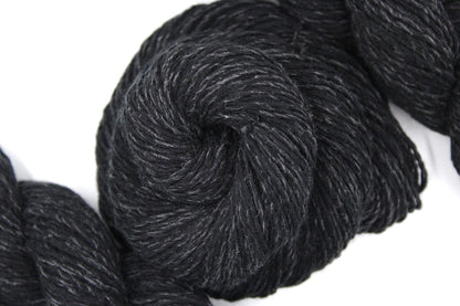 A skein of black and grey, DK weight Yarn recycled by hand from unwanted sweaters swirled attractively in the center of the frame. 