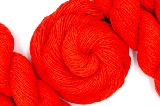 A skein of Bright Orange, Fingering weight Yarn recycled by hand from unwanted sweaters swirled attractively in the center of the frame. 