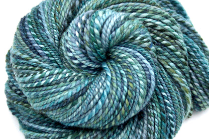 A close up view of a one of a kind, DK Weight, hand dyed variegated skein of multicolored Blue, Teal, and Green self-striping 100% Merino wool Yarn. 