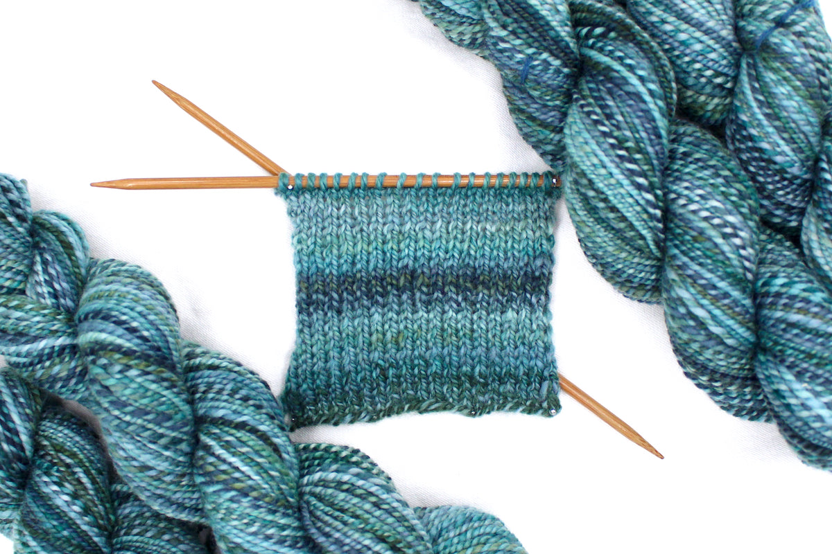 A sample swatch knitted from a one of a kind, DK Weight, hand dyed variegated skein of multicolored O Blue, Teal, and Green self-striping 100% Merino wool Yarn. 