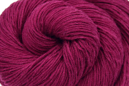 A close up shot of a skein of Maroon, Fingering weight Yarn recycled by hand from unwanted sweaters beautifully coiled in the center of the frame. 