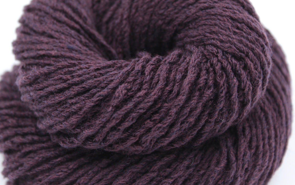 A close up shot of a skein of Dark Maroon, Worsted weight Yarn recycled by hand from unwanted sweaters beautifully coiled in the center of the frame. 