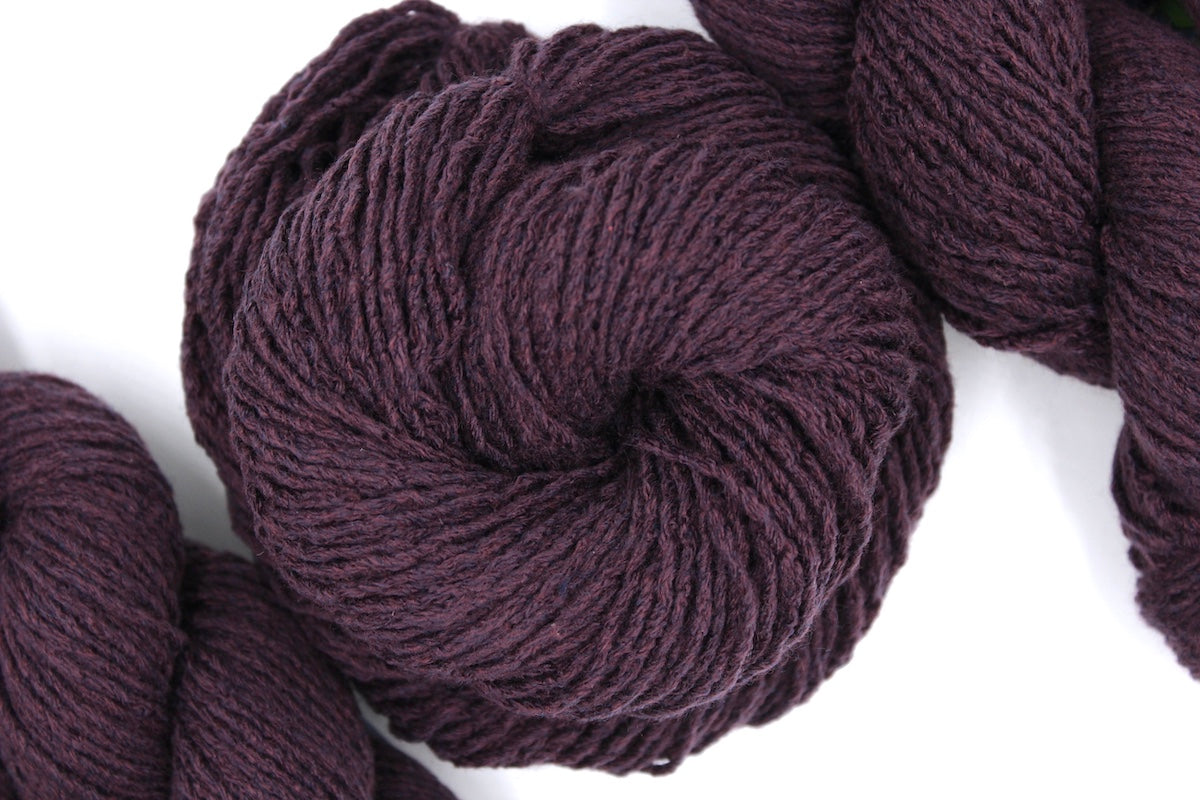 A skein of Dark Maroon, Worsted weight Yarn recycled by hand from unwanted sweaters swirled attractively in the center of the frame. 