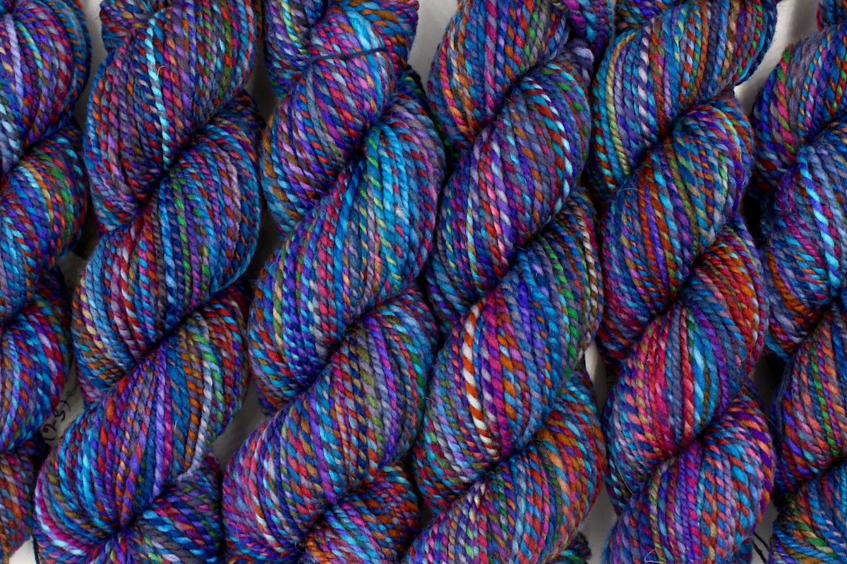 Six one of a kind, hand dyed Variegated skeins of multicolored Rainbow self-striping wool Yarn lined up side by side. 