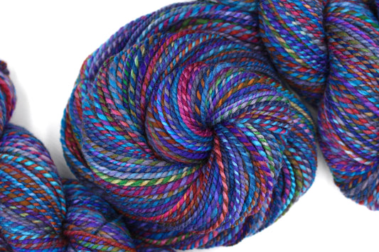 A one of a kind, hand dyed Variegated skein of multicolored Rainbow self-striping wool Yarn coiled attractively in the center of the frame.