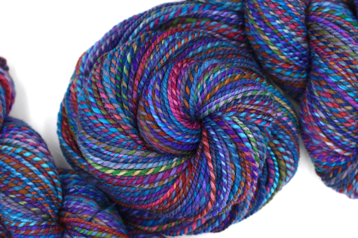 A one of a kind, hand dyed Variegated skein of multicolored Rainbow self-striping wool Yarn coiled attractively in the center of the frame. 