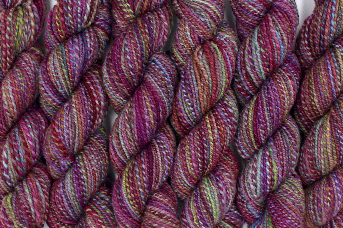 Six one of a kind, hand dyed Variegated skein of multicolored Maroon, Pink, Cornflower Blue, and Lime Green self-striping wool Yarn lined up side by side. 