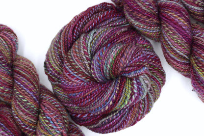 A one of a kind, Dk Weight, hand dyed Variegated skein of self striping Maroon, Pink, Cornflower Blue, and Lime Green Yarn, made of 100% Hand Dyed Merino Wool and coiled attractively in the center of the frame. 