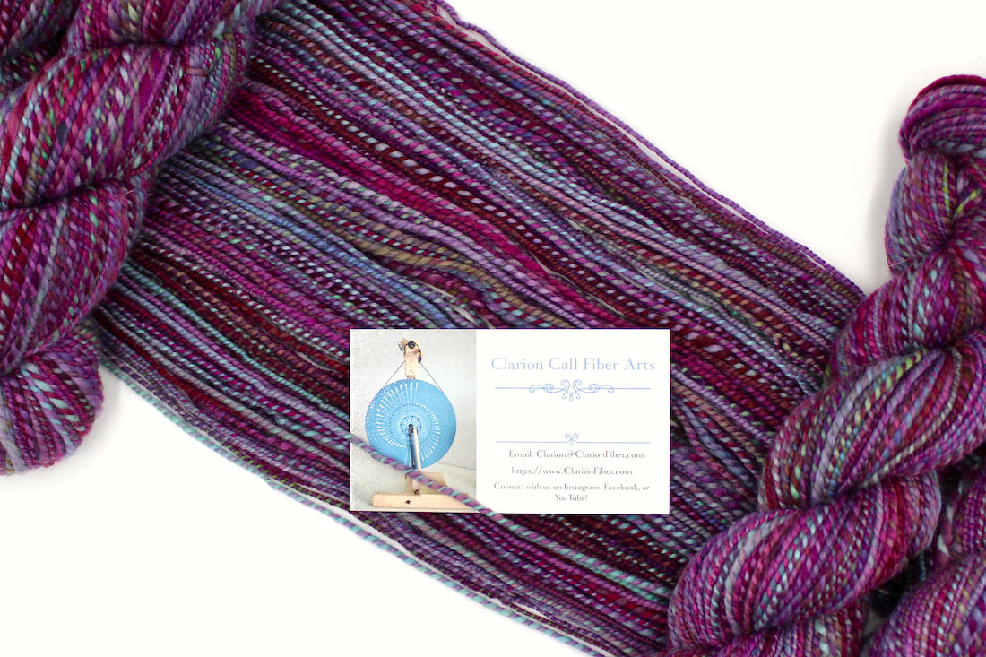 A one of a kind, Dk Weight, hand dyed Variegated skein of self striping Maroon, Pink, Cornflower Blue, and Lime Green Yarn, made of 100% Hand Dyed Merino Wool draped diagonally across the frame, so you can really see the color play. 