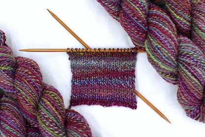 A sample swatch knitted on size 5 knitting needles from a one of a kind, Dk Weight, hand dyed Variegated skein of self striping Maroon, Pink, Cornflower Blue, and Lime Green Yarn, made of 100% Hand Dyed Merino Wool. 