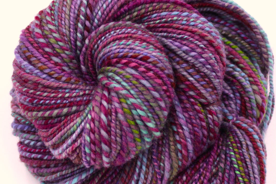 A close up view of a one of a kind, Dk Weight, hand dyed Variegated skein of self striping Maroon, Pink, Cornflower Blue, and Lime Green Yarn, made of 100% Hand Dyed Merino Wool. 