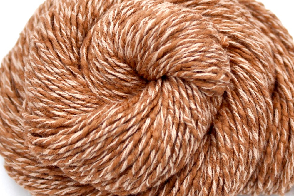 A close up shot of a skein of Muted Orange, Dk weight, Boucle Yarn recycled by hand from unwanted sweaters beautifully coiled in the center of the frame. 