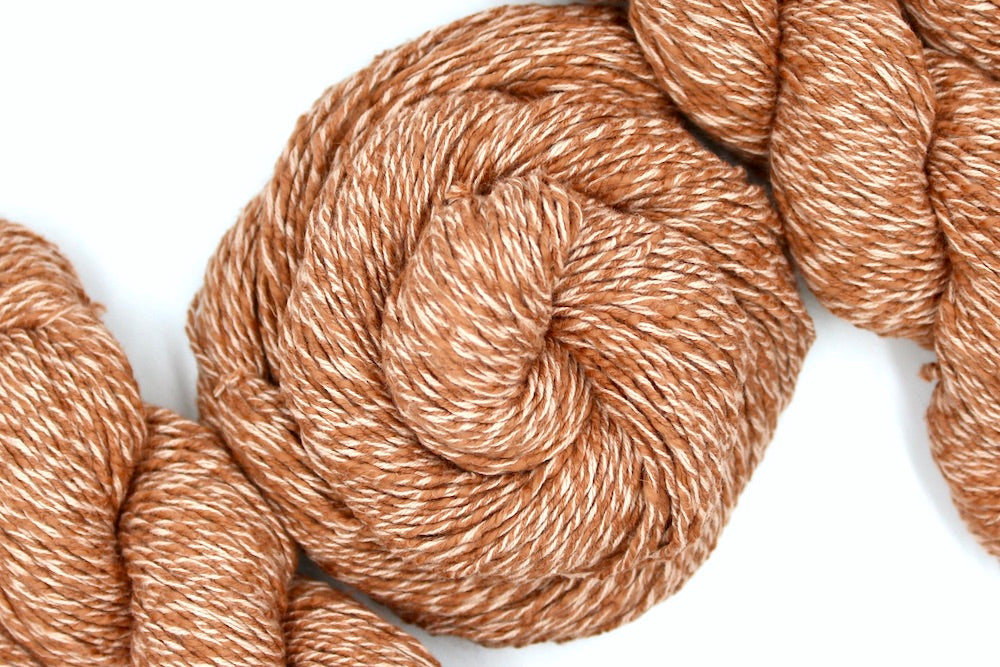 A skein of Muted Orange, Dk weight, Boucle Yarn recycled by hand from unwanted sweaters swirled attractively in the center of the frame. 