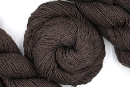 A skein of Vegan, Dark Chocolate Brown, 100% Upcycled Cotton, Heavy Worsted (or Aran) Weight Yarn recycled by hand from unwanted sweaters swirled attractively in the center of the frame. 