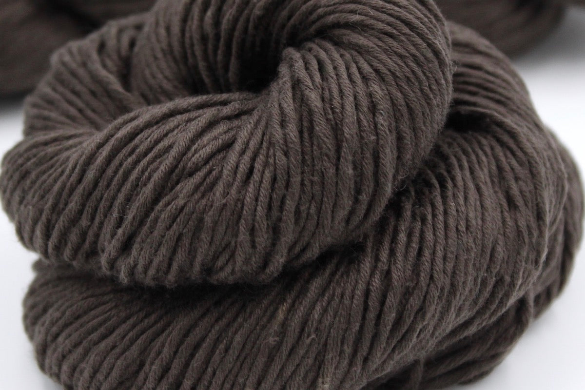 A close up shot of a skein of Vegan, Dark Chocolate Brown, 100% Upcycled Cotton, Heavy Worsted (or Aran) Weight Yarn recycled by hand from unwanted sweaters beautifully coiled in the center of the frame. 