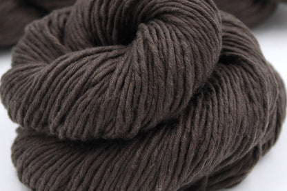 A close up shot of a skein of Vegan, Dark Chocolate Brown, 100% Upcycled Cotton, Heavy Worsted (or Aran) Weight Yarn recycled by hand from unwanted sweaters beautifully coiled in the center of the frame. 