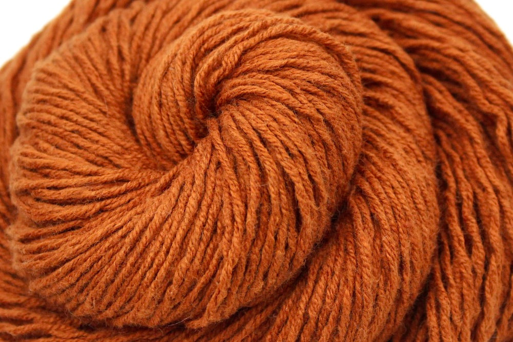 A close up shot of a skein of Brownish Orange, Sport weight Yarn recycled by hand from unwanted sweaters beautifully coiled in the center of the frame. 