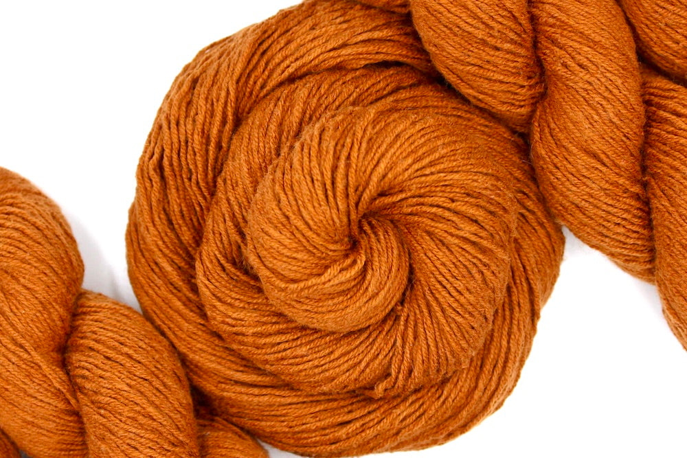 A skein of Brownish Orange, Sport weight Yarn recycled by hand from unwanted sweaters swirled attractively in the center of the frame. 