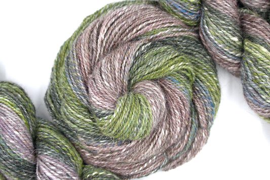 A one of a kind, hand dyed gradient skein of multicolored Dark Forest Green, Lime Green, Cornflower Blue, Mauve, and Grey self-striping wool Yarn coiled attractively in the center of the frame. 