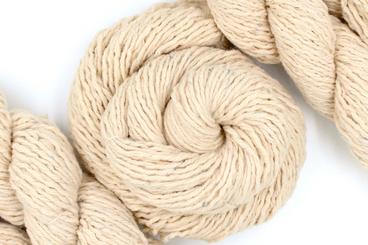 A skein of Beige or Cream, 90% Upcycled Acrylic, 10% Wool, Heavy Worsted (or Aran) Weight Yarn recycled by hand from unwanted sweaters swirled attractively in the center of the frame. 