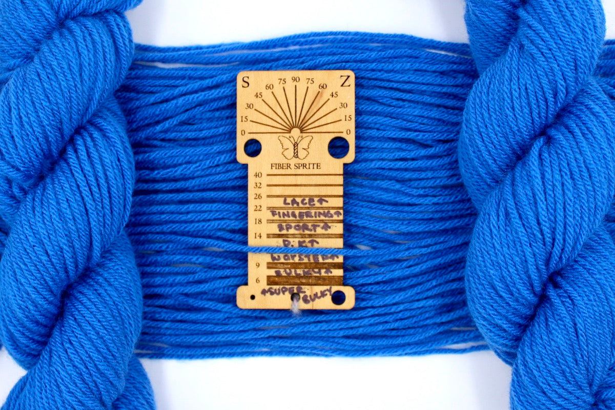 A skein of Royal Blue, Worsted Yarn recycled by hand from unwanted sweaters draped over a Llama shaped Yarn weight tool. 