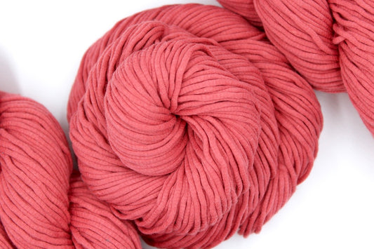 A skein of Coral Pink, Worsted weight Yarn recycled by hand from unwanted sweaters swirled attractively in the center of the frame. 