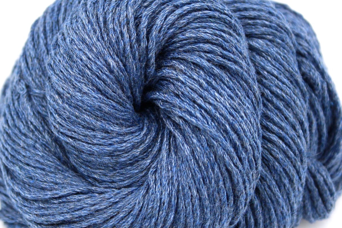 A close up shot of a skein of Cornflower Blue, Dk weight Yarn recycled by hand from unwanted sweaters beautifully coiled in the center of the frame. 