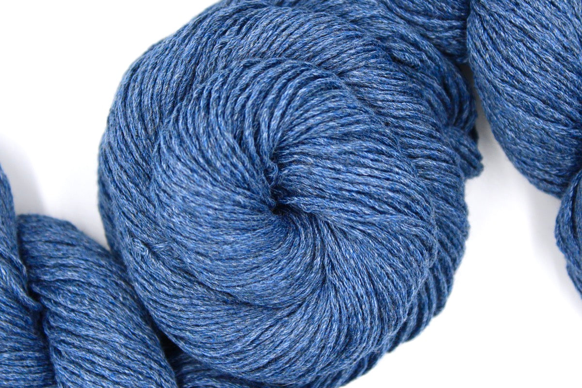 A skein of Cornflower Blue, Dk weight Yarn recycled by hand from unwanted sweaters swirled attractively in the center of the frame. 
