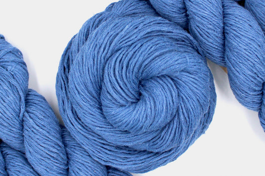 A skein of Vegan, Cornflower Blue, 55% Ramie, 45% Cotton, Worsted weight Yarn recycled by hand from unwanted sweaters swirled attractively in the center of the frame. 