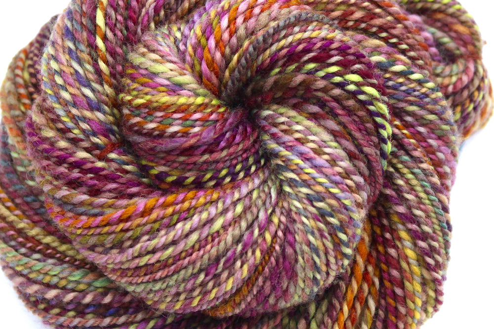 A close up view of a one of a kind, Sport Weight, hand dyed variegated skein of multicolored Red, Orange, Yellow, and Purple self-striping 100% Merino wool Yarn. 