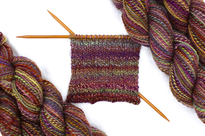A sample swatch knitted from a one of a kind, Sport Weight, hand dyed variegated skein of multicolored Red, Orange, Yellow, and Purple self-striping 100% Merino wool Yarn. 