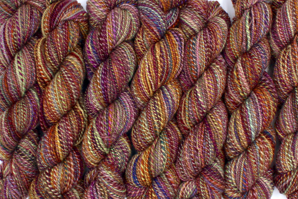 Six one of a kind, Sport Weight, hand dyed variegated skein of multicolored Red, Orange, Yellow, and Purple self-striping 100% Merino wool Yarn lined up side by side. 