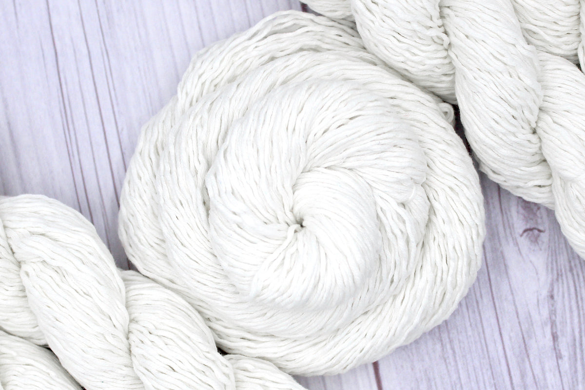 A skein of Vegan, Off-white, 60% Cotton, 40% Acrylic, Sport Weight Yarn recycled by hand from unwanted sweaters swirled attractively in the center of the frame. 