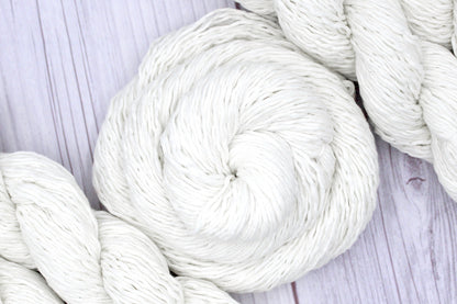 A skein of Vegan, Off-white, 60% Cotton, 40% Acrylic, Sport Weight Yarn recycled by hand from unwanted sweaters swirled attractively in the center of the frame. 