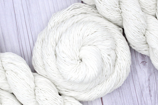 A skein of Vegan, Off-white, 60% Cotton, 40% Acrylic, Sport Weight Yarn recycled by hand from unwanted sweaters swirled attractively in the center of the frame. 