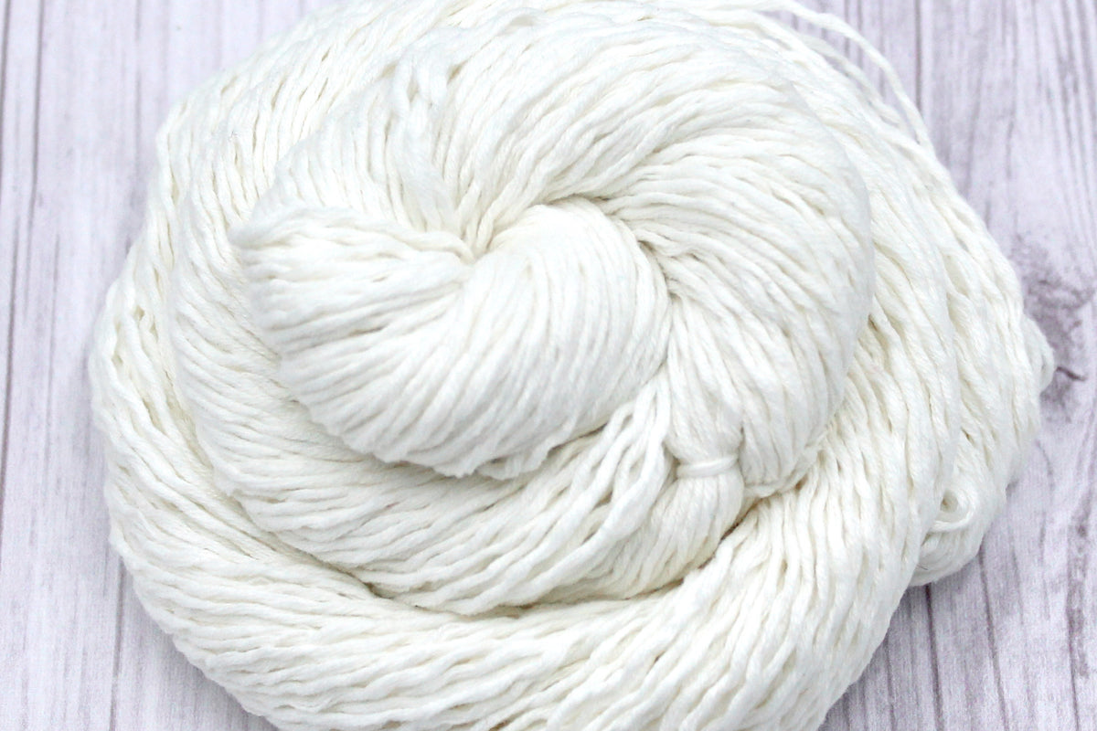 A close up shot of a skein of Vegan, Off-white, 60% Cotton, 40% Acrylic, Sport Weight Yarn recycled by hand from unwanted sweaters beautifully coiled in the center of the frame. 