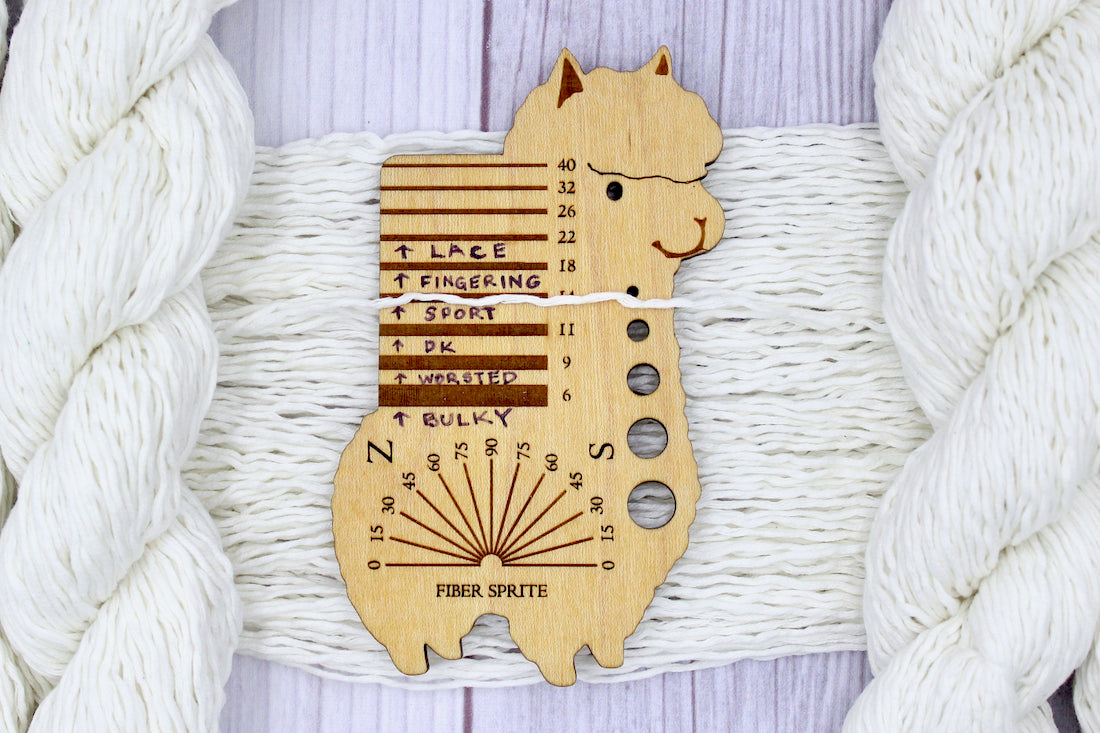 A skein of Vegan, Off-white, 60% Cotton, 40% Acrylic, Sport Weight Yarn recycled by hand from unwanted sweaters draped over the center of the frame with one strand on top of a Llama shaped Yarn weight tool, to better illustrate the thickness of the yarn. 