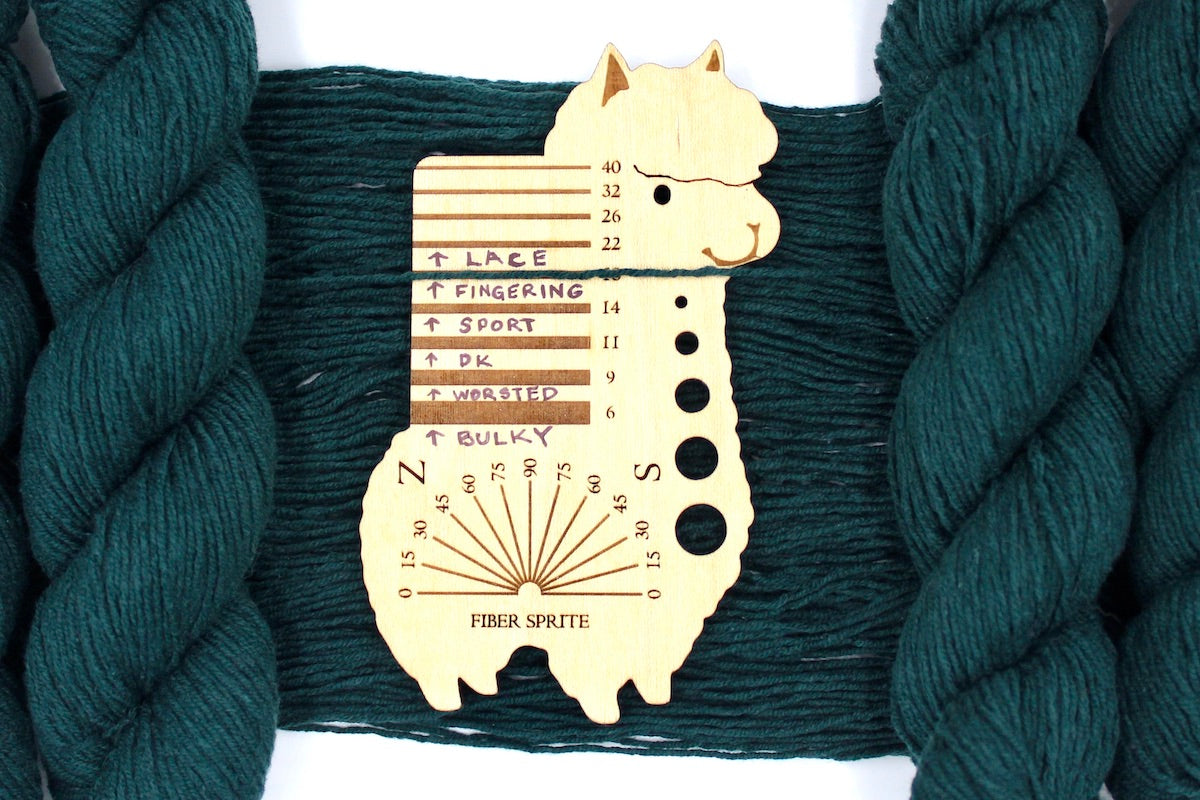 A skein of Dark Forest green, Fingering Yarn recycled by hand from unwanted sweaters draped over a Llama shaped Yarn weight tool. 